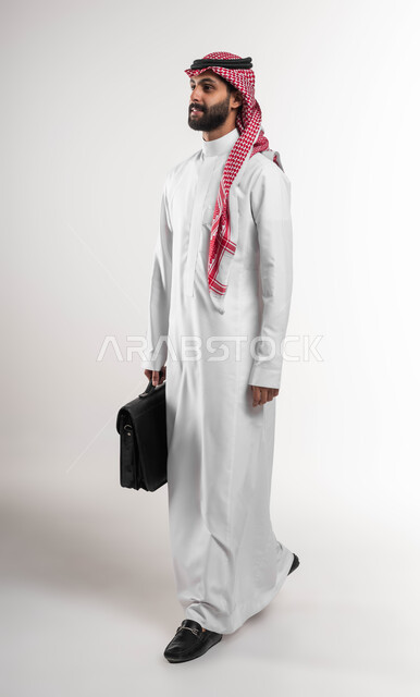 الاهتمام بالأناقة والمظهر الخارجي، الذهاب إلى دوام العمل بنشاط, الشعور بالسرور لتحقيق أهداف الشركة, بورتريه لرجل أعمال عربي سعودي خليجي مبتسم يرتدي الشماغ والثوب التقليدي يحمل حقيبة يد, صورة الجسم بالكامل, خلفية بيضاء