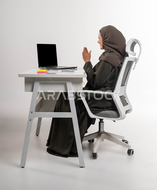 حضور المحاضرات الجامعية أونلاين، مفهوم تطوير المشاريع والخطط المستقبلية، مهن ووظائف نسائية سعودية، إدارة الأعمال المكتبية عبر الأجهزة الحديثة عن بعد، بورتريه لامرأة عربية خليجية سعودية محجبة ترتدي العباءة تقوم بإجراء بث مباشر عبر الحاسب المحمول، خلفية بيضاء