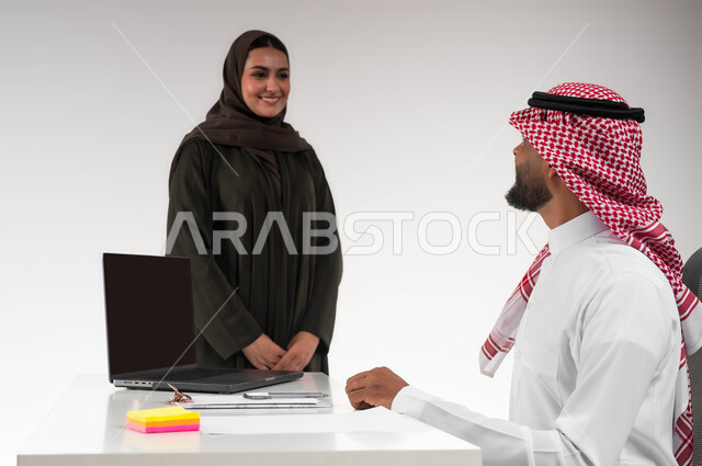 Integrating work with technology and technology, gaining experience and expanding the network of professional relationships, a close-up portrait of two smiling Gulf Arab Saudi colleagues exchanging conversations about successful deals, cooperation and teamwork, directing efforts to achieve the company’s goals, white background.