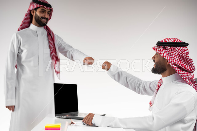 التعارف وبناء علاقات اجتماعية، تبادل الخبرات والاتفاقيات الناجحة، مفهوم الإدارة المتعاونة، بورتريه مقرب لصديقين عربيين خليجيين سعوديين مبتسمين يرتديان الشماغ والثوب التقليدي يقومان بالسلام بقبضة اليد بدون ملامسة، التحية في وباء الكورونا، خلفية بيضاء.