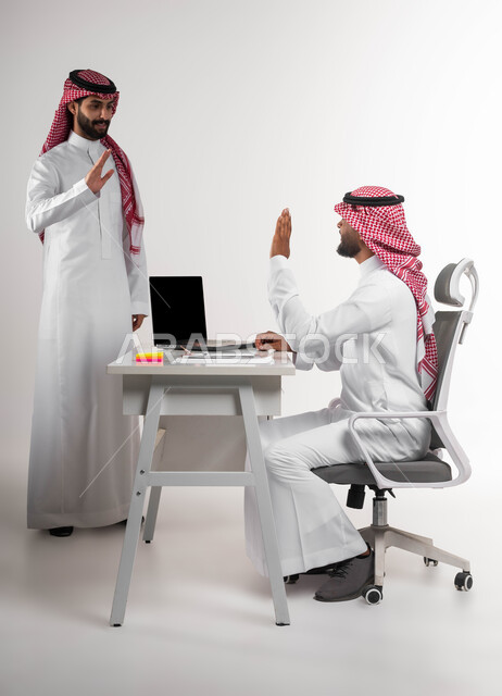 مفهوم الصداقة وبناء علاقات اجتماعية، تبادل الخبرات والاتفاقيات الناجحة، مفهوم الإدارة المتعاونة، بورتريه مقرب لصديقين عربيين خليجيين سعوديين مبتسمين يرتديان الشماغ والثوب التقليدي يقومان بالتلويح باليد والسلام عن بعد، التحية في وباء الكورونا، خلفية بيضاء.
