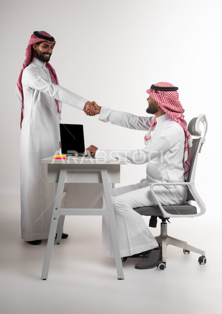Concluding new partnership deals, contracting with various parties to expand the field of work, the concept of cooperative management, a close-up portrait of two Saudi Gulf Arab men wearing the shemagh and traditional thobe, shaking hands with gestures of pleasure at the success of the company’s plan, cooperation and achieving high gains and profits, white background.