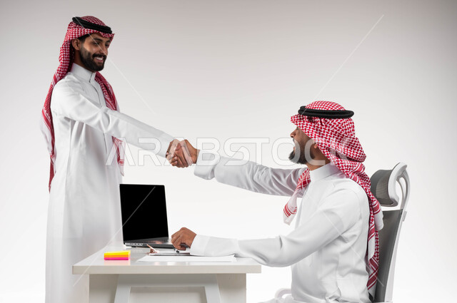 التعاقد مع أطراف متنوعة لتوسيع مجال العمل، مفهوم الإدارة المتعاونة لتحقيق أهداف الشركة، بورتريه مقرب لرجلين عربيين خليجيين سعوديين مبتسمين يرتديان الشماغ والثوب التقليدي يتصافحان بإيماءات السرور بنجاح الصفقة، تحقيق مكاسب و أرباح عالية، خلفية بيضاء.