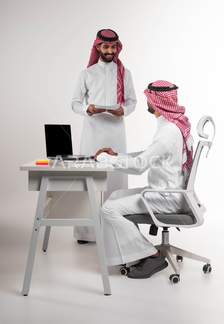 تبادل الخبرات و المهارات في مكتب العمل، بورتريه لموظفين عربيين خليجيين سعوديين يرتديان الشماغ والثوب التقليدي يتناقشان في أمور العمل باستخدام الأوراق والبيانات، التعاون والتفاعل الجماعي لتحقيق أهداف الشركة وحل المشكلات، عرض مزايا صفقة عمل جديدة، خلفية بيضاء