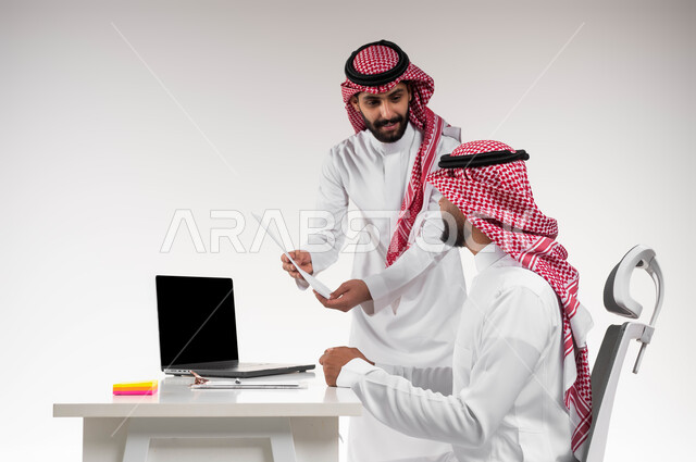 مناقشة أمور العمل باستخدام الأوراق و البيانات، بورتريه مقرب لسيدا أعمال عربيين خليجيين سعوديين مبتسمين يرتديان الشماغ والثوب التقليدي يعقدان صفقة شراكة جديدة، الوحدة والتفاعل الجماعي لتحقيق أهداف الشركة وحل المشكلات، شرح أساليب العمل الجديدة للموظفين، خلفية بيضاء.
