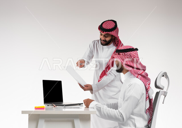 مفهوم الإدارة المتعاونة  لتحقيق أهداف الشركة، بورتريه لموظفين عربيين خليجيين سعوديين يرتديان الشماغ والثوب التقليدي يتناقشان في أمور العمل باستخدام الأوراق، الإشارة الى العقود و الاشراف على التطور المهني، التعاون والتفاعل الجماعي و حل المشكلات، خلفية بيضاء