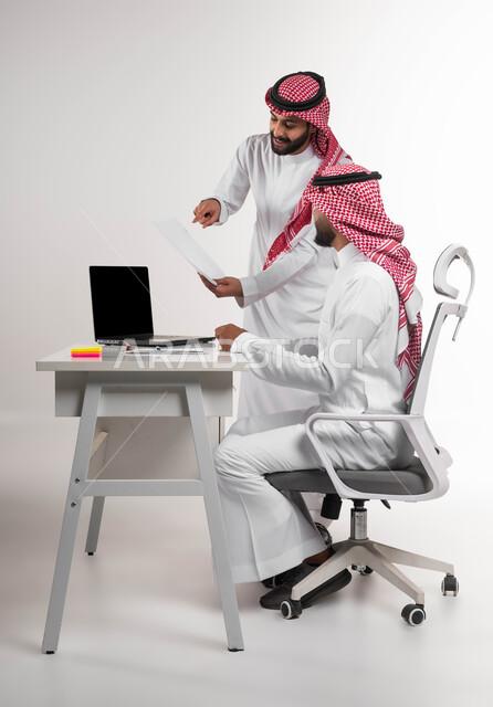 مفهوم الإدارة المتعاونة، الإشارة إلى العقود لدراستها، بورتريه لرجلين عربيين خليجيين سعوديين يرتديان الشماغ والثوب التقليدي يتناقشان في أمور العمل باستخدام الأوراق والبيانات في المكتب، الوحدة والتفاعل الجماعي لتحقيق أهداف الشركة وحل المشكلات، خلفية بيضاء.