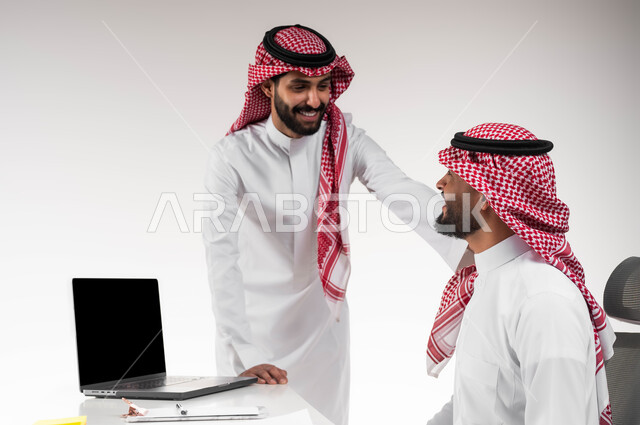 مفهوم الادارة المتعاونة لتحقيق أهداف الشركة وحل المشكلات، الشعور بالإعجاب في الآداء والدعم، بورتريه لرجلي أعمال عربيان خليجيان سعوديان مبتسمان يرتديان الشماغ والثوب التقليدي يتبادلان الحوارات حول صفقة عمل ناجحة بإيماءات السرور، خلفية بيضاء.