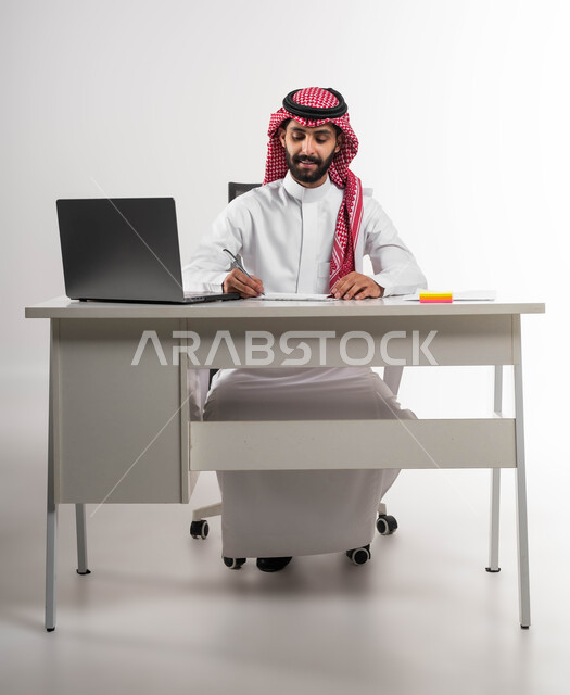 مفهوم الرجولة والثقة بالنفس، شخصية بارزة ومهمة، بورتريه لشاب عربي سعودي خليجي مبتسم يرتدي الشماغ والثوب التقليدي يجلس على كرسي المكتب ويقوم بتنظيم الأمور في الشركة, الاهتمام بالأناقة والمظهر الخارجي، خلفية بيضاء .