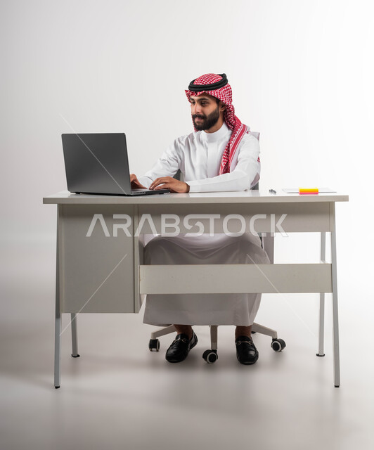إدارة شؤون الأعمال وتنظيمها, النقر والتفاعل مع لوحة المفاتيح, التفكير في استراتيجيات وأهداف العمل، بورتريه لموظف عربي سعودي خليجي يرتدي الشماغ والثوب التقليدي يقوم بالعمل على جهاز اللابتوب المحمول, إيماءات التركيز والتمعن, خلفية بيضاء .