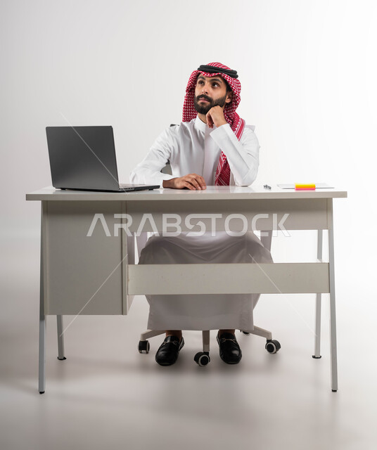 النظر إلى شيء ما في الأعلى, التفكير في استراتيجيات وأهداف العمل، بورتريه لموظف عربي سعودي خليجي يرتدي الشماغ والثوب التقليدي يقوم بالتخطيط والتأمل داخل مكتبه, إيماءات التركيز والتمعن, إدارة شؤون الأعمال وتنظيمها, خلفية بيضاء.