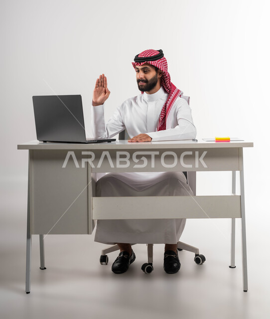 التواصل مع الأهل والأصدقاء, مكالمات فيديو وبث مباشر, التلويح باليد والسلام عن بعد، بورتريه  لرجل عربي سعودي خليجي مبتسم يرتدي الشماغ والثوب التقليدي يقوم باستخدام جهاز الحاسوب المحمول, اجتماعات عمل أونلاين, خلفية بيضاء .