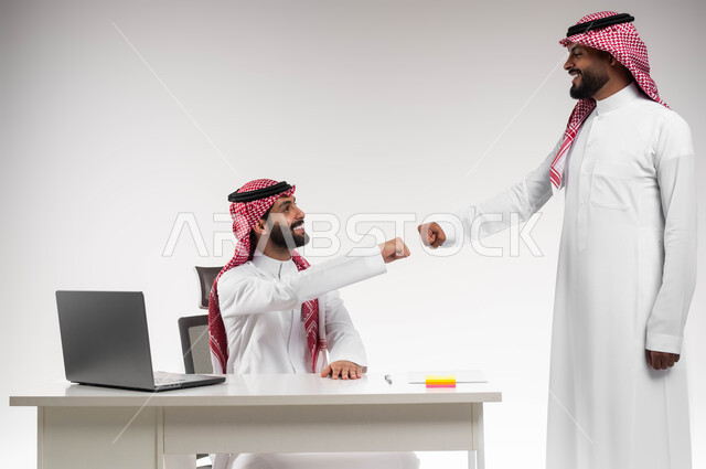 تعابير الصداقة العميقة، تبادل الخبرات والاتفاقيات الناجحة، مفهوم الإدارة المتعاونة، بورتريه لصديقين عربيين خليجيين سعوديين مبتسمين يرتديان الشماغ والثوب التقليدي يقومان بالسلام بقبضة اليد بدون ملامسة، التحية في وباء الكورونا، خلفية بيضاء.