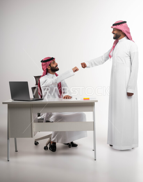 تبادل الخبرات والاتفاقيات الناجحة، تعابير الصداقة العميقة، مفهوم الإدارة المتعاونة، بورتريه لصديقين عربيين خليجيين سعوديين مبتسمين يرتديان الشماغ والثوب التقليدي يقومان بالسلام بقبضة اليد بدون ملامسة، التحية في وباء الكورونا، خلفية بيضاء.