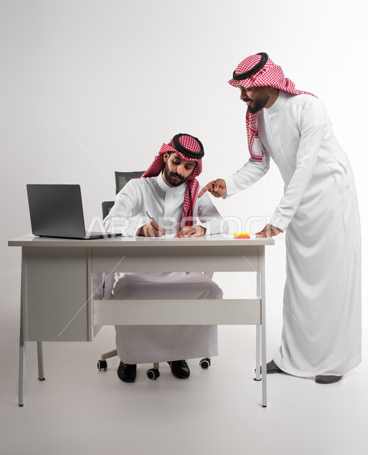 الوحدة والتفاعل الجماعي لتحقيق أهداف الشركة وحل المشكلات، الإشارة إلى العقود لدراستها، مفهوم الإدارة المتعاونة، بورتريه لموظفين عربيين خليجيين سعوديين مبتسمين يرتديان الشماغ والثوب التقليدي يناقشان أمور العمل باستخدام الأوراق والبيانات، خلفية بيضاء.