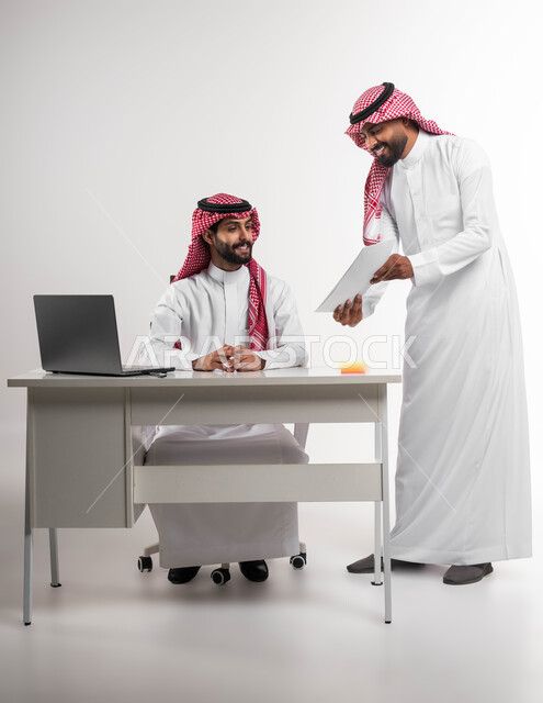عرض مزايا الصفقات الجديدة، مفهوم الإدارة المتعاونة، بورتريه لموظفين عربيين خليجيين سعوديين مبتسمين يرتديان الشماغ والثوب التقليدي يناقشان أمور العمل باستخدام الأوراق والبيانات، الوحدة والتفاعل الجماعي لتحقيق أهداف الشركة وحل المشكلات، خلفية بيضاء.