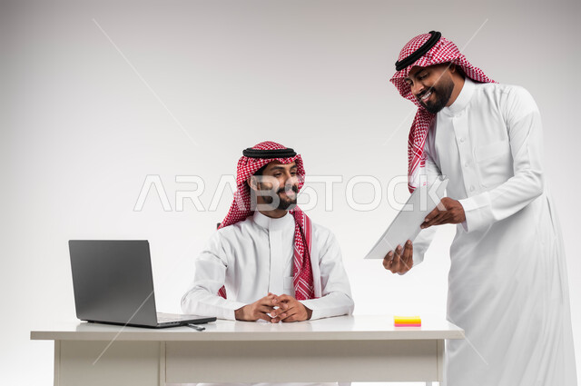 مفهوم الإدارة المتعاونة، بورتريه لموظفين عربيين خليجيين سعوديين مبتسمين يرتديان الشماغ والثوب التقليدي يناقشان أمور العمل باستخدام الأوراق والبيانات، إنجاز المهام المكتبية اليومية، الوحدة والتفاعل الجماعي لتحقيق أهداف الشركة وحل المشكلات، خلفية بيضاء.