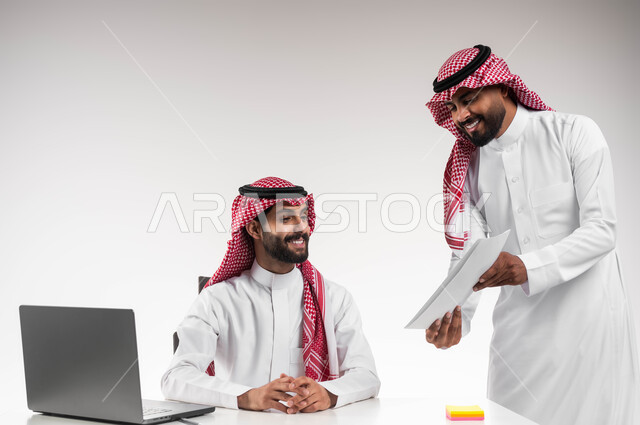 عرض مزايا الصفقات الجديدة، مفهوم الإدارة المتعاونة، بورتريه لرجلان عربيان خليجيان سعوديان مبتسمان يرتديان الشماغ والثوب التقليدي يناقشان أمور العمل باستخدام الأوراق والبيانات، الوحدة والتفاعل الجماعي لتحقيق أهداف الشركة وحل المشكلات، خلفية بيضاء.