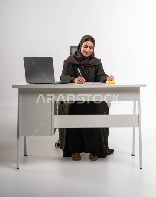تدقيق المشاريع والمخططات، تنظيم الأمور في الشركة بإيماءات السرور, مفهوم الثقة بالنفس والانوثة، إعداد خطط الاعمال الاستراتيجية, شخصية سعودية بارزة مهمة، بورتريه لامرأة عربية خليجية سعودية ترتدي العباءة والحجاب تجلس وراء الطاولة وتقوم بتدوين الملاحظات ،خلفية بيضاء