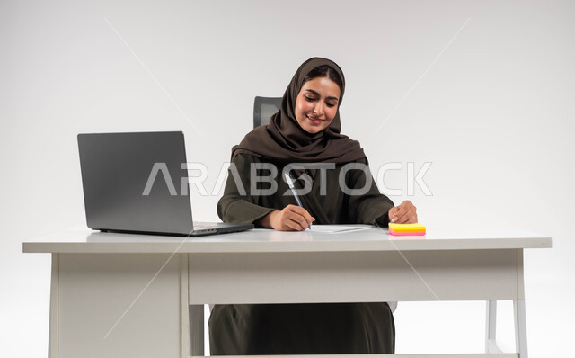 تنظيم الأمور في الشركة بإيماءات السرور, مفهوم الثقة بالنفس والانوثة، إعداد خطط الاعمال الاستراتيجية, شخصية سعودية بارزة مهمة، بورتريه لامرأة عربية خليجية سعودية محجبة ترتدي العباءة السوداء تقوم بتدوين الملاحظات، تدقيق المشاريع والمخططات، خلفية بيضاء