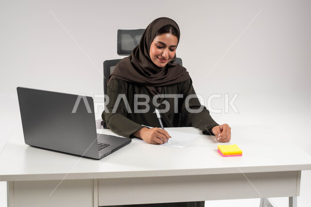 إعداد خطط الاعمال الاستراتيجية, تنظيم الأمور في الشركة بإيماءات السرور, مفهوم الثقة بالنفس والانوثة، شخصية سعودية بارزة مهمة، بورتريه لامرأة عربية خليجية سعودية محجبة ترتدي العباءة السوداء وتقوم بتدوين الملاحظات، تدقيق المشاريع والمخططات، خلفية بيضاء