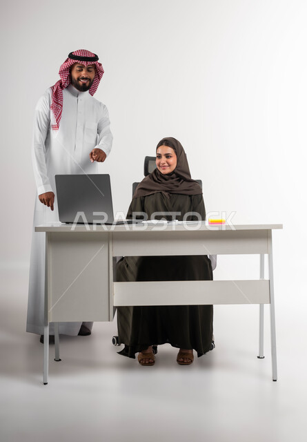 الاشارة الى الحاسوب المحمول للانتباه للملاحظات وتطبيقها، العمل الجماعي وروح الفريق الواحد، متابعة إنجازات مهام الموظفين، بورتريه لرجل وامرأة عربيين خليجيين سعوديين يقومان بتطوير الخطط لتحقيق أهداف الشركة، صورة الجسم بالطول الكامل، خلفيه بيضاء