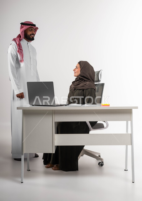 تبادل الدردشات حول الصفقات الناجحه بإيماءات السرور، الشعور بالإعجاب في الآداء والدعم، مفهوم الإدارة المتعاونة، بورتريه لسيدة أعمال عربية خليجيه سعودية محجبة مع السكرتير الخاص بها في مقر الشركة، استخدام التقنيات الحديثة، بيئة عمل مريحة و ناجحة، خلفية بيضاء