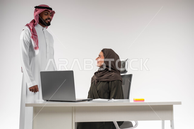 مفهوم الإدارة المتعاونة، تبادل الاحاديث حول الصفقات الناجحه بإيماءات السرور، الشعور بالإعجاب في الآداء والدعم، بورتريه لسيدة أعمال عربية خليجيه سعودية محجبة مع السكرتير الخاص بها في مقر الشركة، استخدام التقنيات الحديثة، بيئة عمل مريحة و ناجحة، خلفية بيضاء