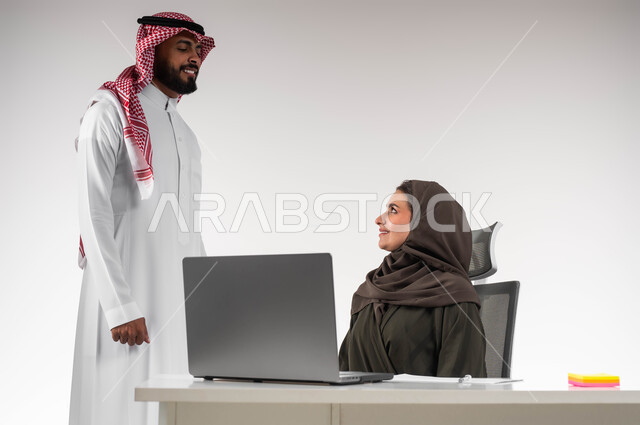 تبادل الاحاديث حول الصفقات الناجحه بإيماءات السرور، الشعور بالإعجاب في الآداء والدعم، بورتريه لسيدة أعمال عربية خليجيه سعودية محجبة مع السكرتير الخاص بها في مقر الشركة، مفهوم الإدارة المتعاونة، استخدام التقنيات الحديثة، بيئة عمل مريحة و ناجحة، خلفية بيضاء