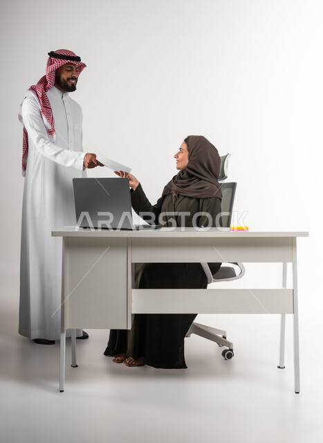 تسليم المشروع بالوقت اللازم، تحقيق أهداف الشركة بالوقت المطلوب، إدارة شؤون الأعمال وتنظيمها، بورتريه لموظف عربي خليجي يرتدي الزي التقليدي يقوم بتقديم الأوراق لمديرته بإيماءات السرور، بيئة عمل مريحة و ناجحة، صورة الجسم بالطول الكامل، خلفية بيضاء