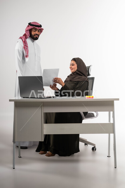 متابعة ومناقشة المشاريع، مهن و أعمال تجارية، سييدة أعمال عربيه خليجية سعودية محجبة مع موظف سعودي يقومان بمراجعه المخططات و القواعد الاساسية بإيماءات السرور، استخدام التقنيات الحديثة، تحقيق اهداف الشركة المطلوبة، العمل الجماعي وروح الفريق الواحد، خلفيه بيضاء