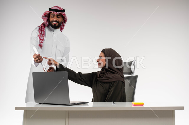 تعليم الموظفين الأساليب الجديدة لتحقيق الأهداف المطلوبة، العمل الجماعي وروح الفريق الواحد، بورتريه لزميلين عربيين سعوديين خليجيين يقومان بمناقشة و تنظيم الاعمال داخل مقر الشركة، الاشارة إلى الاوراق و الاشراف على التطور المهني للمهام، خلفية بيضاء