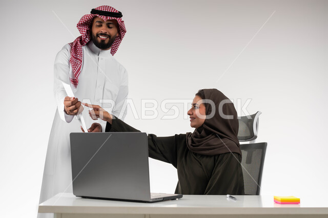 العمل الجماعي وروح الفريق الواحد، بورتريه لزميلين عربيين سعوديين خليجيين يقومان بمناقشة و تنظيم الاعمال داخل مقر الشركة، تعليم الموظفين الأساليب الجديدة لتحقيق الأهداف المطلوبة، الاشارة إلى الاوراق و الاشراف على التطور المهني للمهام، خلفية بيضاء