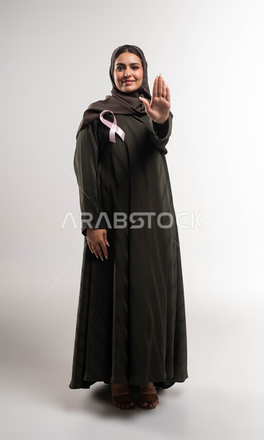 طلب المنع والتوقف عن إهمال الكشف المبكر، حملة توعوية عن سرطان الثدي، بورتريه لإمرأة عربية خليجي سعودية مبتسمة ترتدي الحجاب والعباءة تضع الشريط الوردي ترفع يدها بحركات الرفض والقوة، تحدي الأمراض الخبيثة، رمز الحملة العالمية، صورة الجسم بالكامل، خلفية بيضاء