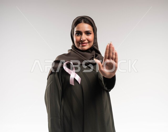 المنع والتوقف عن إهمال الكشف المبكر، حملة توعوية عن سرطان الثدي، بورتريه مقرب لإمرأة عربية خليجي سعودية مبتسمة ترتدي الحجاب والعباءة تضع الشريط الوردي ترفع يدها بحركات الرفض والقوة، تحدي الأمراض والأورام الخبيثة، رمز الحملة العالمية، خلفية بيضاء