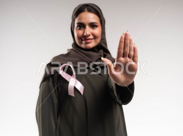 القيام بحملة توعوية عن سرطان الثدي، المنع والتوقف عن إهمال الكشف المبكر، بورتريه مقرب لإمرأة عربية خليجي سعودية مبتسمة ترتدي الحجاب والعباءة تضع الشريط الوردي ترفع يدها بحركات الرفض والقوة، تحدي الأمراض والأورام الخبيثة، رمز الحملة العالمية، خلفية بيضاء
