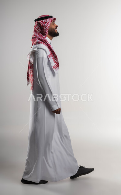 الذهاب الى مكان ما بتعابير وإيماءات الحماس والسرور، بورتريه من الجانب لرجل عربي سعودي خليجي مبتسم يرتدي الشماغ والثوب التقليدي يقوم بالمشي للذهاب إلى العمل، الاهتمام والاعتناء بالمظهر الخارجي، صوره الجسم بالطول الكامل, خلفية بيضاء