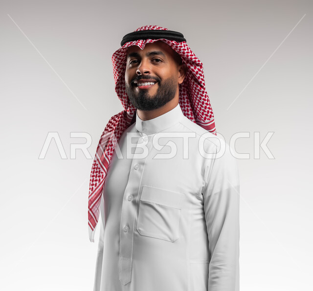 الاهتمام بالمظهر الخارجي، بورتريه مقرب لرجل عربي خليجي سعودي مبتسم يرتدي الشماغ والثوب السعودي التقليدي ينظر إلى الكاميرا بتعابير السرور، ايماءات الثقة والاعتزاز بالنفس، مفهوم الاناقه والرجولة، الوقوف باستقامة وانضباط، خلفية بيضاء