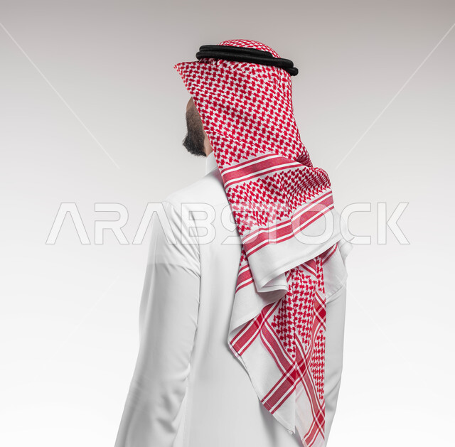 A display of Saudi men’s clothing brands, attention and care for the external appearance, a close-up portrait from the back of a Saudi Gulf Arab man wearing a shemagh and a traditional thobe, looking at something, adornment, beautification and arrangement, white background.