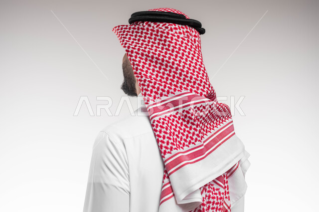 التزين و التجمل و الترتيب, عرض ثياب الماركات الرجالية السعودية، الاهتمام والاعتناء بالمظهر الخارجي، بورتريه مقرب من الخلف لشاب عربي خليجي سعودي يرتدي الشماغ والثوب التقليدي ينظر الى شيء ما، خلفية بيضاء