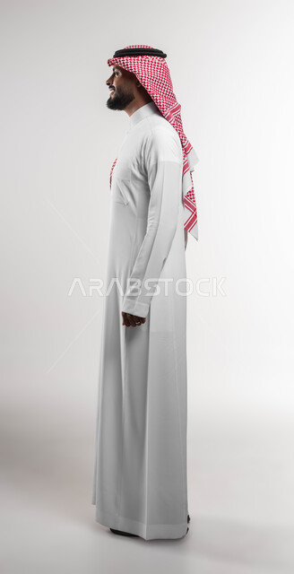الاهتمام والاعتناء بالمظهر الخارجي، بورتريه من الجانب لشاب عربي خليجي سعودي مبتسم يرتدي الشماغ والثوب التقليدي ينظر الى شيء ما بتعابير السرور والسعادة، التزين و التجمل و الترتيب, عرض ثياب الماركات الرجالية السعودية، صورة الجسم بالطول الكامل، خلفية بيضاء