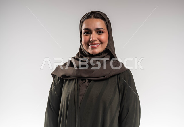 مفهوم الأنوثة والنعومة, الوقوف بابتسامة وثقة بالنفس, صورة شخصية للوثائق الرسمية, بورتريه مقرب لإمرأة عربية خليجية سعودية ترتدي العباءة والحجاب تنظر إلى الكاميرا بإيماءات السرور والسعادة, خلفية بيضاء