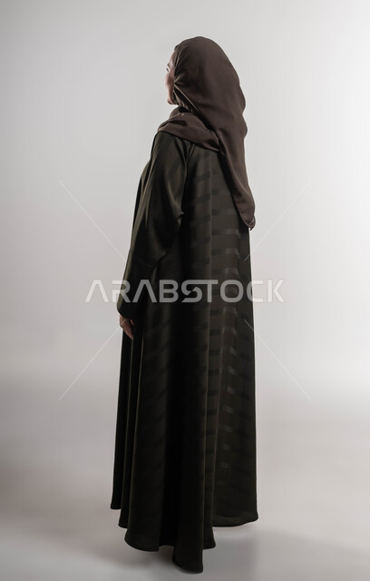 النظرة المستقبلية والتفكير لتحقيق النجاح, التمعن وإيجاد حل لموضوع ما, بورتريه من الخلف لإمرأة عربية خليجية سعودية ترتدي العباءة والحجاب تنظر إلى شيء ما, صورة الجسم بالطول الكامل, خلفية بيضاء