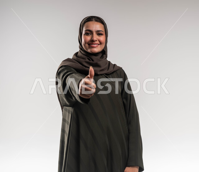النجاح وتحقيق أهداف الشركة, الرضا والإعجاب والقبول, بورتريه مقرب لسيدة أعمال عربية خليجية سعودية مبتسمة ترتدي العباءة والحجاب ترفع يديها بإيماءات الجودة والامتياز, مهن ووظائف نسائية سعودية, خلفية بيضاء