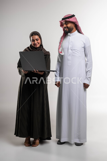 العمل الجماعي وروح الفريق الواحد, تعلم اساليب العمل والتطوير المهني عبر الحاسب المحمول، بورتريه لزميلين عربيين خليجيين سعوديين يقومان بمناقشة المهام والأعمال، تطوير الخطط وحل المشكلات لتحقيق أهداف الشركة، صورة الجسم بالطول الكامل، خلفيه بيضاء