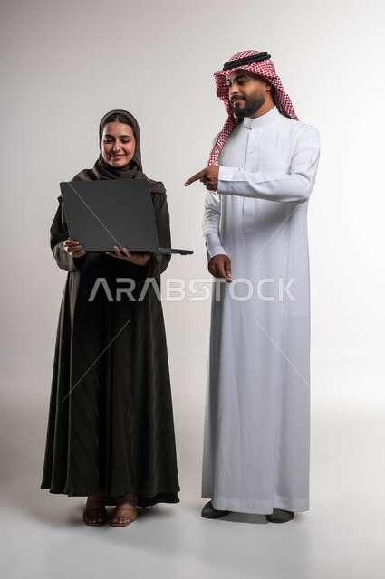 Learn work methods and professional development via the laptop, a portrait of two Saudi Gulf Arab colleagues discussing tasks and work, developing plans and solving problems to achieve the company’s goals, teamwork and team spirit, full-length body photo, white background.
