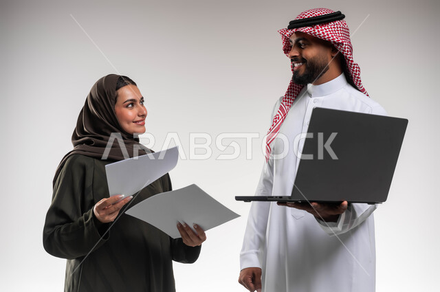 تبادل الأفكار والخبرات لتحقيق أهداف العمل، التعاون وروح الفريق الواحد، بورتريه مقرب لزميلين عربيين سعوديين خليجيين يقومان بمناقشة و تنظيم الاعمال بإستخدام جهاز الحاسوب المحمول، دمج العمل مع التقنية والتكنولوجيا، تطوير استراتيجيات العمل، خلفية بيضاء.
