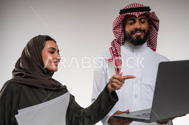 تعليم الموظفين الأساليب الجديدة في العمل لتحقيق أهداف الشركة، دمج العمل مع التقنية والتكنولوجيا، بورتريه مقرب لزميلين عربيين خليجيين سعوديين مبتسمين يقومان بإنجاز المهام عبر الحاسوب المحمول، الاشارة الى اللابتوب، العمل الجماعي وروح الفريق الواحد، خلفيه بيضاء