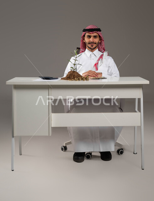 النهضة والنمو الاقتصادي في المملكة, التعامل بالعملات الورقية والمعدنية في السعودية, بورتريه لرجل عربي خليجي سعودي مبتسم يرتدي الثوب التقليدي والشماغ ينظر إلى الكاميرا بإيماءات السرور, مفهوم الوفرة المالية, الإحصائيات والحسابات البنكية, خلفية رمادية