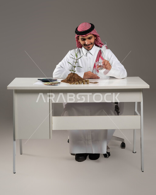 Financial abundance and the concept of saving, national metal and silver coins, using a calculator to postpone calculations, finance, investment and economic projects, a portrait of a smiling Saudi Arabian Gulf man wearing a traditional thobe and shemagh holding a piggy bank in his hand, gray background